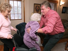 Joe Fauteux, right, helps his mother-in-law, Madelyn Reitzel, 89, into her wheelchair with the help of Madelyn's daugther, Jeannie Fauteux, left., 2014.  The family was told that the care they receive by CCAC will be cut to one hour a day. (DAX MELMER/The Windsor Star)