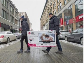 Two men are shown carrying a large screen television across a street in Montreal on December 26, 2013 after buying it during a Boxing Day sale. (Canadian Press files)
