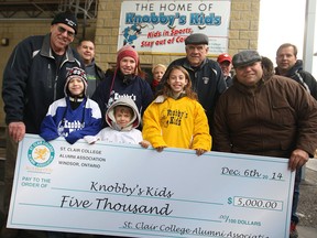 Knobby's Kids, front row from left, Noah Villeneuve, 9, Caleb Villeneuve, 7, Zoe Villeneuve, 10, and Benjamin Villeneuve, 7, centre are joined by Knobby's Kids co-founders, Frank Spry, far left, and Jerry Slavik, second from right, as well as St. Clair College Alumni Association president, Serge Bertucci, far left, as well as alumni board members at Lanspeary Park, Monday, Dec. 1, 2014. Knobby's Kids received a $5000 cheque from the St. Clair College Alumni Association to cover ice time costs and insurance for the season. (DAX MELMER/The Windsor Star)