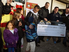irefighter Sean Costello (centre left) is presented with a cheque for $5500 by Dan Michos from Elite Roofing for Sparky's Toy Drive in Windsor on Friday, December 19, 2014. Elite Roofing collected $10,000 in toys and clothes in addition to the money.   (TYLER BROWNBRIDGE/The Windsor Star)