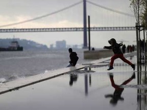 A young boy jumps over a puddle by the Tagus riverbank, in Lisbon, Sunday, Jan. 18, 2015. At the background is the April 25th bridge, whose name was given after the Carnations revolution that restored the democracy in Portugal in April 1974.