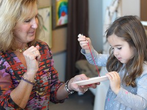 Early years educator Janet Benson helps Sienna Arundine with a sewing exercise when St. Clair College fashion design students meet kindergarten fashionistas at David Suzuki public school in Windsor. (DAN JANISSE/The Windsor Star)