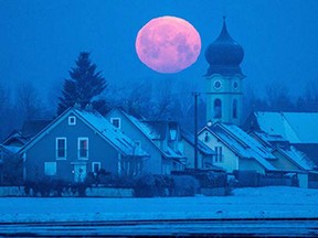 Full moon sets behind the parish church of Schoenach near Regensburg, southern Germany, on February 4, 2015.