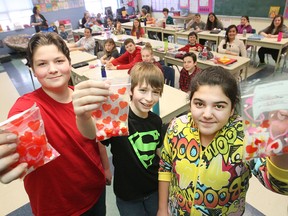 Grade 7 students, from left, Domenic Forget, 12, Andrew Seguin, 12, and Isabella Gallucci, 12, hold up candy grams with their class pictured behind them at St. John Vianney Catholic School, Friday, Feb. 13, 2015.  The grade seven class organized a fundraiser with money going towards Kristine Marchand, a secretary that died unexpectedly from an undiagnosed brain aneurysm.   (DAX MELMER/The Windsor Star)