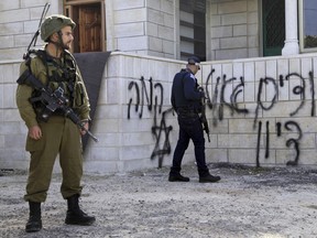 Israeli security forces stand outside a mosque vandalized and torched by suspected Israeli extremists in the village of Jabaa, near Bethlehem, Wednesday, Feb. 25, 2015. Hebrew graffiti at right reads: "we want the redemption of Zion," and "revenge," on the left. (AP Photo/Mahmoud Illean)