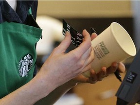 Holly Ainslie, a barista at a Starbucks store in Seattle puts a "Race Together" sticker on a customer's cup, Wednesday, March 18, 2015. Starbucks CEO Howard Schultz announced earlier in the day at the company's annual shareholder meeting that participating baristas at stores in the U.S. will be putting the stickers on cups and also writing the words "#RaceTogether" for customers in an effort to raise awareness and discussion of race relations.
Photograph by: Ted S. Warren , Ottawa Citizen