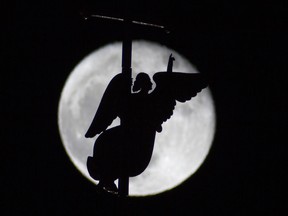 In this photo taken through a telescope lens, the city landmark, a weather vane in the form of an Angel, is fixed atop a spire of the Saints Peter and Paul Cathedral, as it is silhouetted on the rising moon in St.Petersburg, Russia, Tuesday, Jan. 6, 2015. Orthodox Christians are beginning their Christmas celebrations Tuesday. (AP Photo/Dmitry Lovetsky)