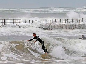 A surfer rides a wave close to a wall as he takes advantage of the large surf created with wild weather hitting Sydney, Australia, Wednesday, April 22, 2015. A fierce storm lashing Australia's southeast destroyed homes, left dozens stranded in swirling floodwaters and may have led to the deaths of three people officials said Tuesday.