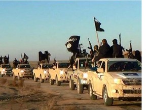 Militants of the Islamic State group hold up their weapons and wave its flags on their vehicles in a convoy on a road leading to Iraq, while riding in Raqqa city in Syria. (Militant website via AP)