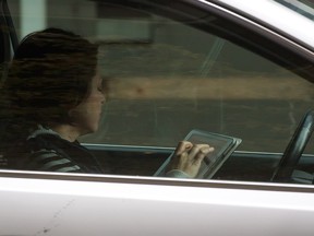 In this file photo, a woman uses an iPad while behind the wheel of a vehicle stopped in traffic at a red light in downtown Vancouver, B.C., on Monday October 20, 2014. Tougher distracted driving penalties came into effect Monday with three penalty points being added to the record of drivers caught talking on a handheld device while driving in addition to a $167 fine. Drivers ticketed for texting while driving previously already received three penalty points, along with a fine of $167. THE CANADIAN PRESS/Darryl Dyck