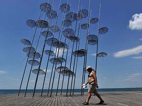 A bare-chested man walks past a modern artwork named "Umbrellas" in the port of Thessaloniki, Greece on June 16, 2015. A mini heatwave with temperatures of 38 degrees Celsius will hit Greece this week. In some areas, temperatures may reach even 40° C weather experts forecast. AFP PHOTO /SAKIS MITROLIDISSAKIS MITROLIDIS/AFP/Getty Images