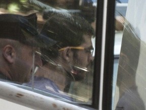 A file picture taken on June 19, 2015 shows a Cypriot policeman escorting a 26-year-old Lebanese-Canadian suspect, Hussein Bassam Abdallah, into a police van following a court appearance in the coastal city of Larnaca. Abdallah pleaded guilty on June 29, 2015 to terror charges linked to 8.2 tonnes of potential bomb-making material found in his Cyprus home, authorities said. (IAKOVOS HATZISTAVROU/Getty Images)