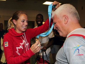 Melissa Bishop, left, gives University of Windsor track head coach Dennis Fairall, right, the gold medal Bishop won in the 800 metres at Pan American Games Thursday July 23, 2015.  Bishop arrived at Windsor Airport to a celebration with friends, teammates and coaches. (NICK BRANCACCIO/The Windsor Star)