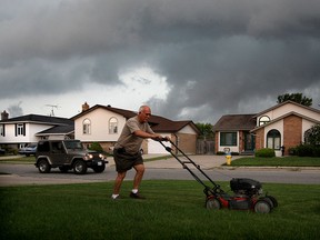 Gaspre Fallea of Heritage Estates in LaSalle, hurries to cut his grass as a storm looms on the western horizon Wednesday July 29, 2015.  Many residents of Heritage Estates have had a problem with flooding and Fallea reports a recent heavy rainfall flooded the 1800 block of Heatherstone Way located to the side of his home. (NICK BRANCACCIO/The Windsor Star)