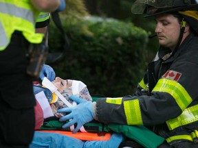 A firefighter tends to a woman after a car crashed into a home in the 1200 block of Ypres Avenue on Saturday, July 25, 2015. (DAX MELMER/The Windsor Star)