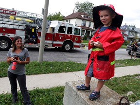 Wearing his own fire hat and coat, Tyler Fairhurst, 5, has a good vantage point as Windsor firefighters respond to a two-vehicle collision on Crawford Avenue near Wyandotte Street West September 9, 2015.  Tyler's mother Becky Fairhurst watches her son, who likes to chase emergency responders when they visit the neighbourhood. (NICK BRANCACCIO/The Windsor Star)
