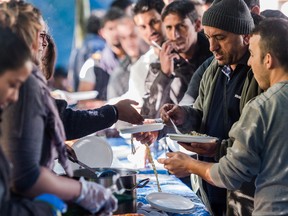 People receive food in a tent camp for refugees and migrants in Brussels on Thursday, Sept. 10, 2015. While recent arrivals to the Office for Migration have been offered lodging in a nearby building, many have still chosen to stay in the park in tents. (AP Photo/Geert Vanden Wijngaert)