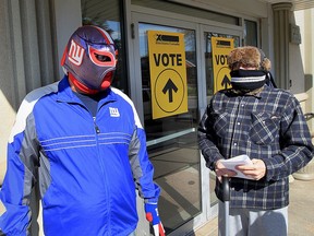 Scott Andrews, right, wore a scarf and full winter hat while voting at polling station on Hanna Street East Monday October 19, 2015. Another man, left, wore New York Giants football team mask covering his entire face while voting in the federal election.