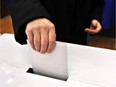 Close-up of a man's hand putting his vote in the ballot box. Photo by fotolia.com.