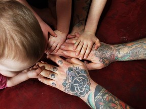 The tattooed hands of Jesse Eldredge are shown with his children at his Windsor, Ont. home.