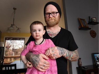 Jesse Eldredge and his daughter Daisy, 2, are pictured in their Windsor, Ont. home. Eldredge once planned on never getting tattooed below his elbows, but the tattoos now extend onto his hands.
