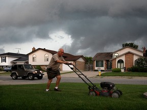 Gaspre Fallea of Heritage Estates in LaSalle, hurries to cut his grass as a storm looms on the western horizon Wednesday, July 29, 2015.  Many residents of Heritage Estates have had a problem with flooding and Fallea reports a recent heavy rainfall flooded the 1800 block of Heatherstone Way located to the side of his home.
