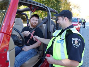 Windsor police Const. Jason Boudreau hands a MADD Campaign ribbon to motorist Matt Walley during a R.I.D.E. spot check to kick off the 2015 Mothers Against Drunk Driving red ribbon campaign.  Windsor Police, Ontario Provincial Police,  LaSalle Police and Amherstburg Police and local fire agencies participated in the event.