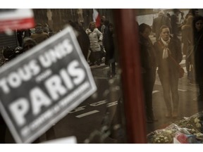 People are reflectied in the shopwindow of Le Carillon restaurant, a site of last Friday's attacks, in Paris, Tuesday, Nov. 17, 2015 . Bar and restaurant owners are urging people to return to their local nightspots Tuesday, relaying the message online and on social media with the slogan "Tous au bistrot" -- Everyone to the bistro. At left reads: All united for Paris.