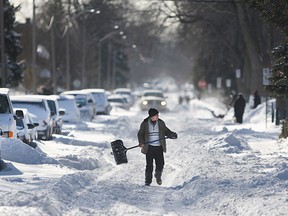 A man walks down the middle of the street with a snow shovel in this February 2015 file photo.