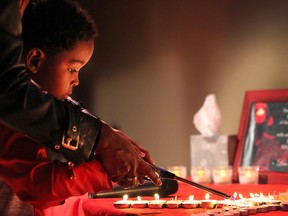 The AIDS Committee of Windsor held a World AIDS Day candlelight vigil on Tuesday, Dec. 1, 2015, at the Capitol Theatre in Windsor, Ont. Isaiah Berhane, 6, helps his mother Salem Berhane light a candle during the event in memory of a person who has died of AIDS.