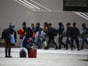 Greek police escort migrants to a van outside a former Olympic indoor stadium in Faliro, southern Athens, on Wednesday, Dec. 16, 2015. Hundreds of people have been temporarily housed in the stadium after being removed a few days ago from Greece's northern border with Macedonia, which only allows Syrians, Afghans and Iraqis through on their trek to wealthier European countries - rejecting others as economic migrants who do not merit refugee protection.