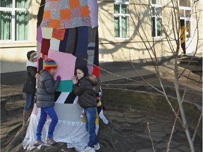 Kids hug a tree covered by knitted  materials, at their school in Ghent, Belgium, Monday, March 4, 2013. The school wants to show their affection for the sole tree in the schoolyard by giving it a coat for the winter.