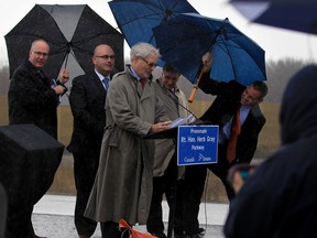 Honourable Marc Garneau, at podium, Minster of  Transport and Hon. Steven Del Duca, behind, Ontario Minister of Transport, unveil a plaque honouring Rt. Hon. Herb Gray during a heavy rainstorm on the Hon. Herb Gray Parkway Monday, Dec. 14, 2015.