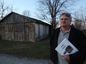 Chris Carter holds up a copy of his book Tour Olinda in front of an old barn in Edgar Mills, one of the “lost communities” that he writes about in another of his books, Tour Essex: The Lost Communities. - John Chan photo