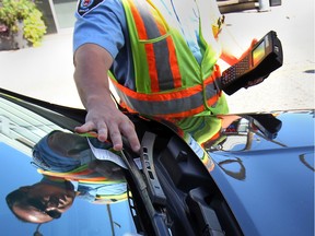 In this file photo, a bylaw enforcement officer tickets a car in downtown Windsor, ON. on Thursday, August 14, 2014.