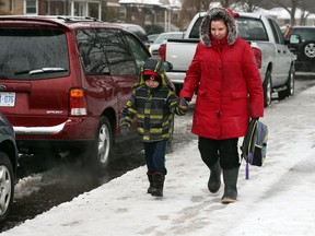 Sarah Baltzer walks her son Colby, 5, past a row of illegally parked vehicles at St. James Catholic Elementary School Wednesday Feb. 24,2016. Parents and grandparents are concerned over expensive parking tickets issued to vehicles which "double park" for about 20 minutes.