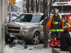 A firefighter walks by a Chevy minivan that jumped the curb on University Avenue West in downtown Windsor, driving onto the sidewalk and knocking down a lamp post.