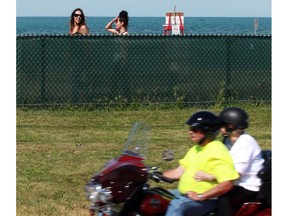 Windsor, Ontario. June 03, 2016. With only their heads visible, Danielle Renaud, 24, left, and Maria Borges, 28, walk on the beach side of a chain link fence which was installed to deter rubberneckers on Riverside Drive East at Sand Point beach June 03, 2016.  (NICK BRANCACCIO/Windsor Star)