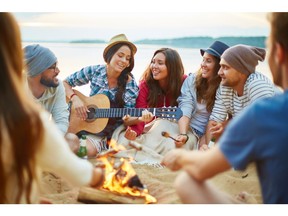 Friends singing and hanging out by campfire. Photo by Getty Images.