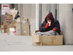 Homeless man in a cardboard box having a warm drink. Poverty image by Getty Images.