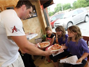 Steve Brown, left, hands out free slices of pizza to Stephanie Allen, Lauren Allen and Chelsea Allen (left to right) in this June 27, 2013 file photo.