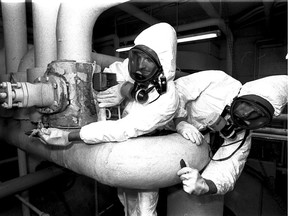 Cocooned like astronauts or deep-sea divers, Scott Inverarity, left, and Stephen Samson work on asbestos cleanup at Forster School on Aug. 2, 1990.