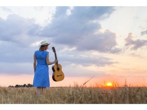 Young woman walking in wheat field with guitar at sunset. Photo by Getty Images.