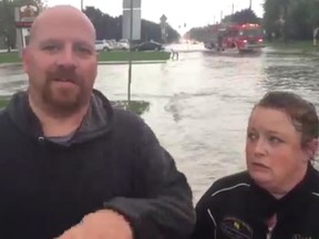 Standing in ankle-deep water with sirens blaring in the background, a couple talks about severe flooding in Tecumseh is delaying their efforts to plan for the funeral of a loved one.