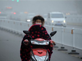 TOPSHOT - A woman rides a scooter down a polluted street while wearing a face mask in Bozhou, in eastern China's Anhui province on December 24, 2015. Ten Chinese cities were on red alert for smog on December 24, state media reported, as large swathes of the country suffered through their fourth wave of choking pollution this month.     CHINA OUT