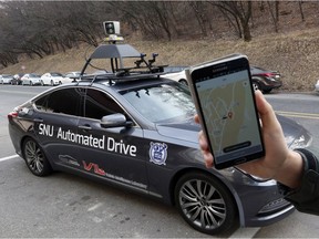A researcher from the Intelligent Vehicle IT Research Center at Seoul National University shows the smartphone application for the driverless car called Snuber with a fixture on its roof with devices that scan road conditions at Seoul National University's campus in Seoul, South Korea, Tuesday, Jan. 5, 2016.