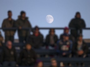A near full moon rises behind the crowd watching the senior boys AA football semi-final between Sandwich Secondary School and Essex District High School at Alumni Field, Friday, Nov. 11, 2016.