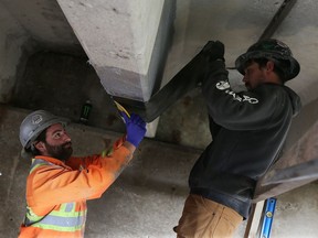 Luke Young, left, and Cory Garno apply a new restoration method to the under side of a bridge on County Road 8 in Essex County on Nov. 14, 2016. The process was developed with the help of University of Windsor students.