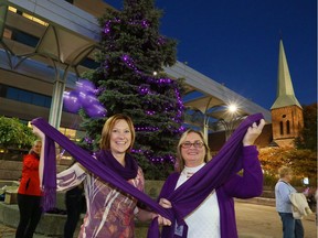 In this file photo from 2016, Shine the Light on Woman Abuse campaign co-ordinator Karry Plaskitt, left, and 2016 honouree and woman abuse speaker Debra Fowler hold purple infinity scarves in front of tree lit with purple lights at Charles Clark Square on Nov. 1, 2016.