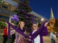 Shine the Light on Woman Abuse campaign co-ordinator Karry Plaskitt, left, and 2016 honouree and woman abuse speaker Debra Fowler hold purple infinity scarves in front of tree lit with purple lights at Charles Clark Square on Nov. 1, 2016.